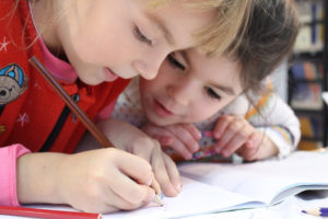 two elementary school children writing in a journal together