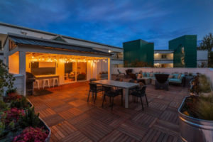 rooftop lounge in evening with rooftop garden, tables, couches, and playful lighting